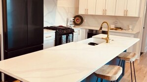 Een moderne keuken met een zwarte koelkast, witte kasten, een blauw kookeiland met barkrukken en een gasfornuis.