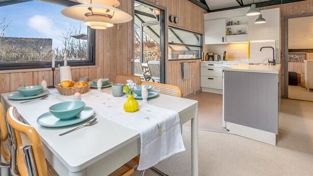 Una cucina moderna con mobili bianchi, un'area pranzo con tavolo apparecchiato per due e vista sull'esterno.