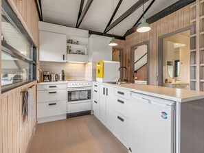 A modern kitchen with white cabinetry, a built-in oven, a stove, and a large island with a sink. - "Lasse" - 550m from the sea by Interhome (Knebel)