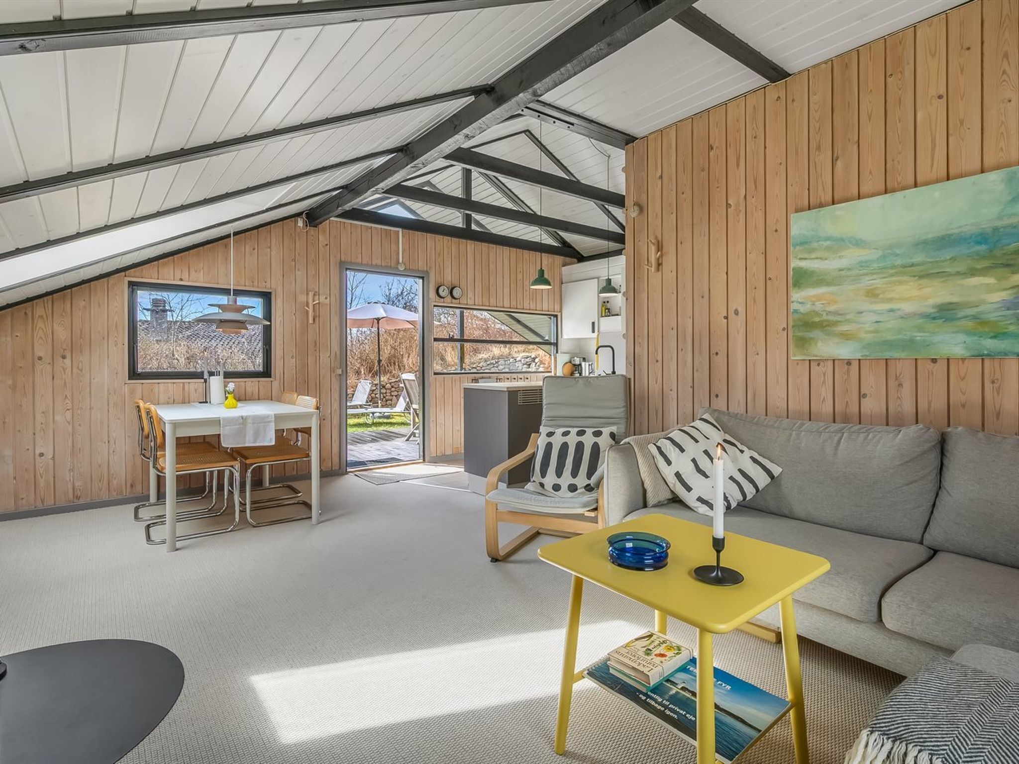 Ein modernes Loft mit hohen Decken, Holzwänden, einem Essbereich, einer Couch und einem Gemälde.
