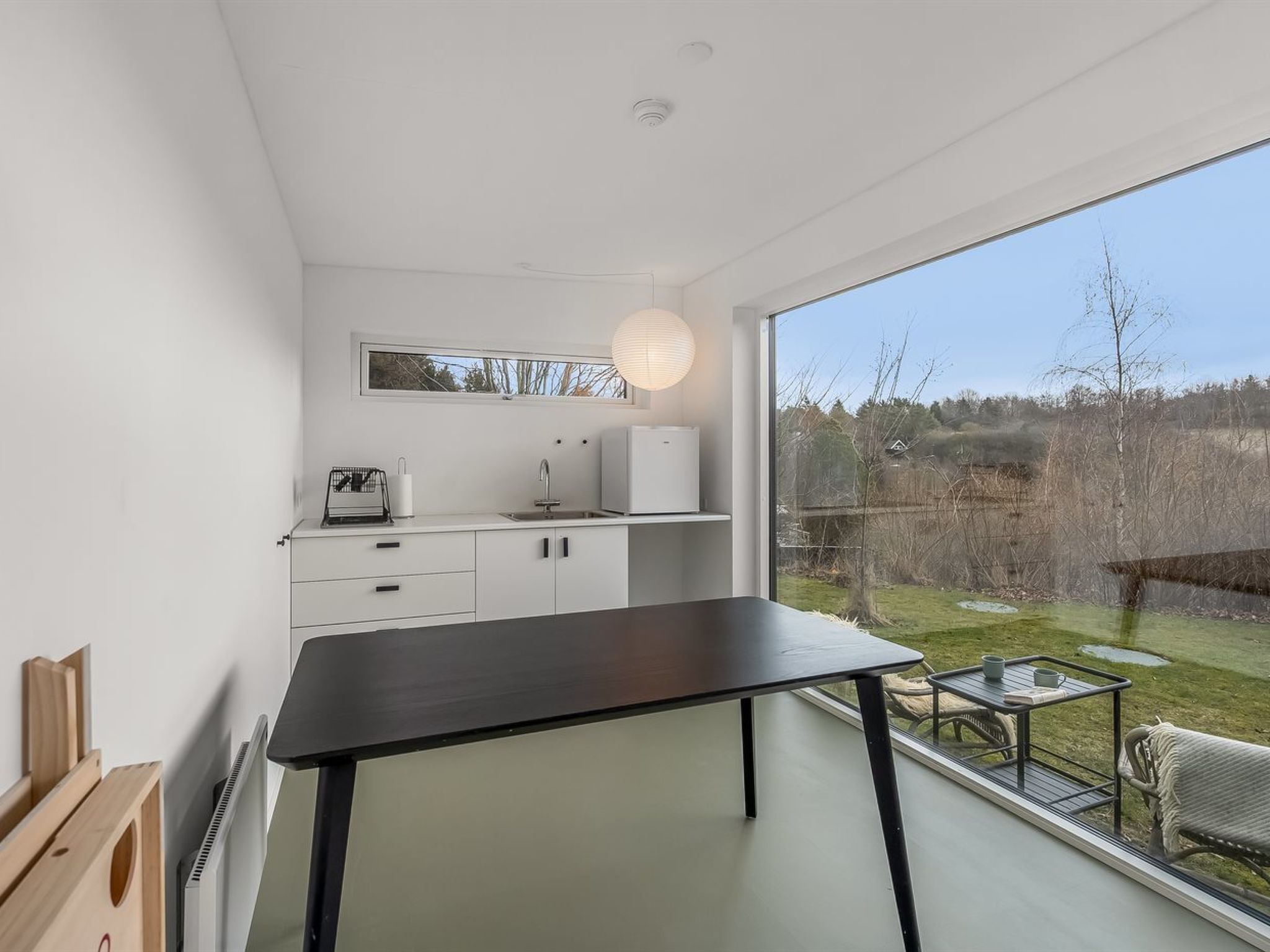 A modern kitchen with white cabinets, a black countertop, and a large window overlooking a garden.