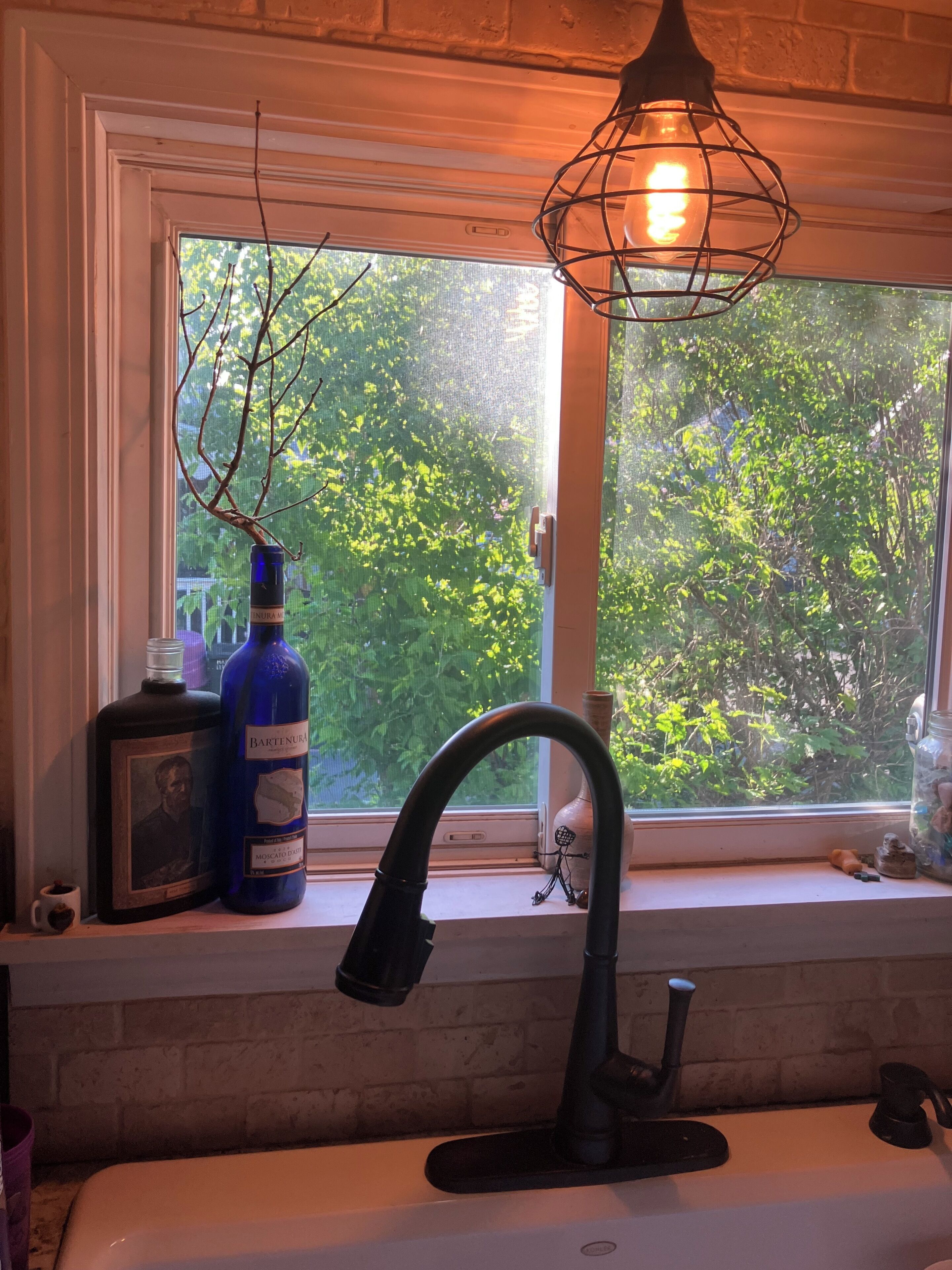 Une cuisine avec une fenêtre, une bouteille et un vase posés sur le rebord de la fenêtre.