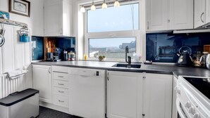 Una cucina moderna con mobili bianchi, una lavastoviglie Bosch, un bollitore nero e una finestra con vista sulla città.