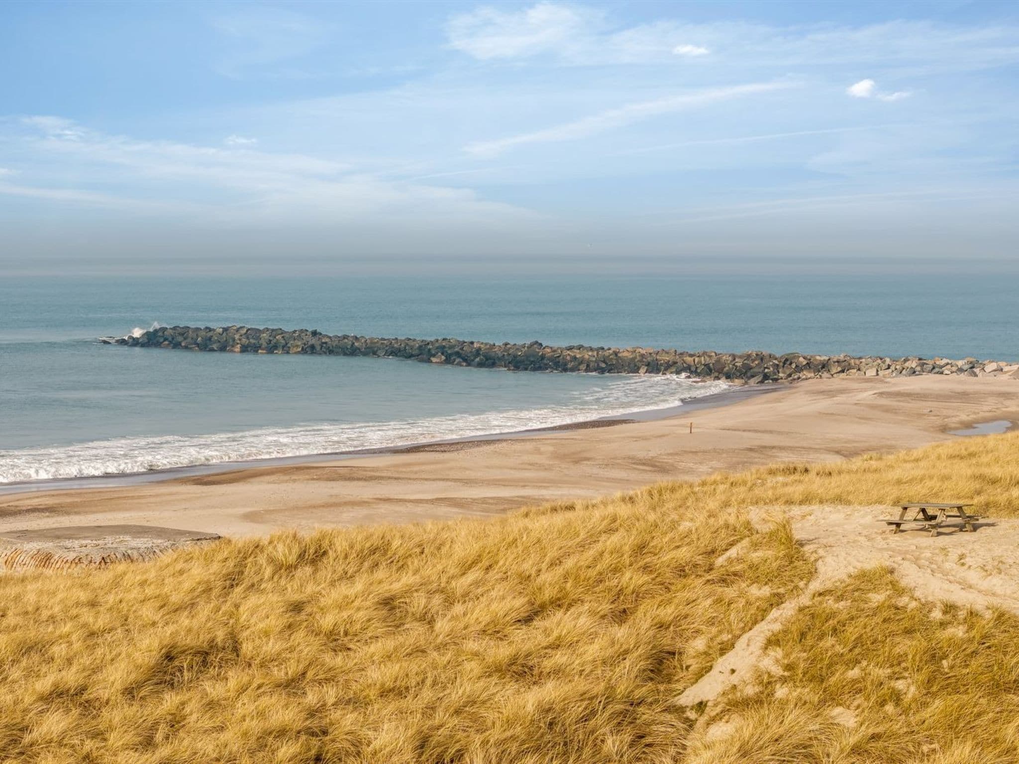 A beach with a rocky breakwater, sandy shore, and grassy dunes.
