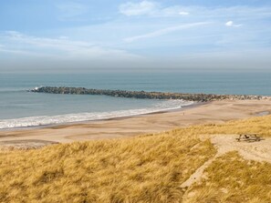 Ein Strand mit einem steinernen Wellenbrecher, sandigem Ufer und grasbewachsenen Dünen.