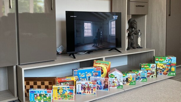 A modern living room with a flat-screen TV, wooden cabinets, and children's toys.