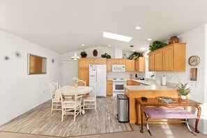 A modern kitchen with wooden cabinets, a dining area with a white table and chairs, and a small island with a bench.