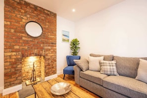 A living room with a brick fireplace, a round mirror, a blue chair, a grey sofa, and a wooden coffee table.