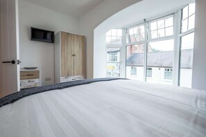 A bedroom with a large bed, a wardrobe, a television, and a window with a view of buildings.