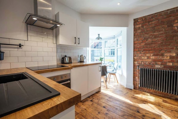 A modern kitchen with white cabinets, a wooden countertop, and a brick wall.