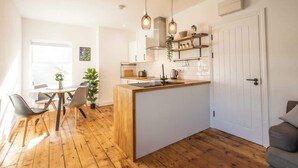 A modern kitchen with a central island, wooden flooring, pendant lighting, and a dining area with chairs. - Ty Llwyd Ceibwr - Modern apartment (Saint Dogmaels)