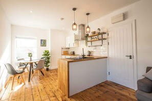 Une cuisine moderne dotée d’un îlot central, de planchers en bois, de luminaires suspendus et d’un coin repas avec des chaises.