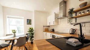 A modern kitchen with a wooden dining table, chairs, a black countertop, a sink, and a window. - Ty Llwyd Ceibwr - Modern apartment (Saint Dogmaels)