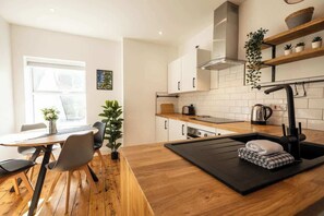 Une cuisine moderne avec une table à manger en bois, des chaises, un plan de travail noir, un évier et une fenêtre.