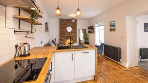 A modern kitchen with a wooden countertop, white cabinets, a brick accent wall, and pendant lighting. - Ty Llwyd Ceibwr - Modern apartment (Saint Dogmaels)
