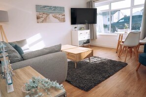 Una sala de estar con sofá, mesa de centro, televisor y vistas al exterior.