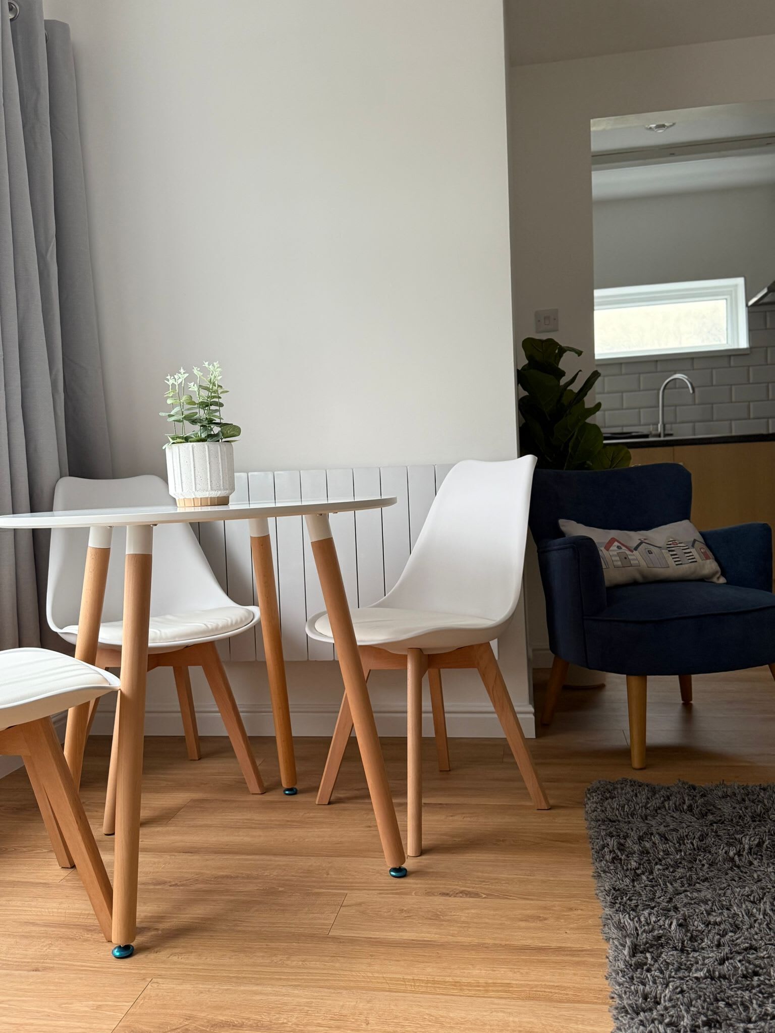 A modern living room with a dining table, chairs, a blue sofa, and a kitchen area in the background.