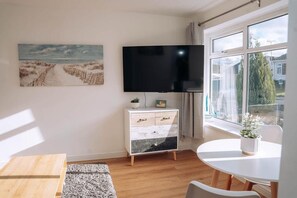 Una sala de estar moderna con un televisor de pantalla plana, un mueble blanco, una mesa de comedor y un ventanal grande.