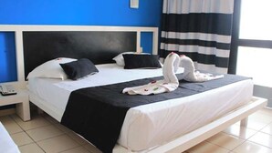 Una habitación de hotel con cama, mesita de noche, teléfono y ventana con cortinas.