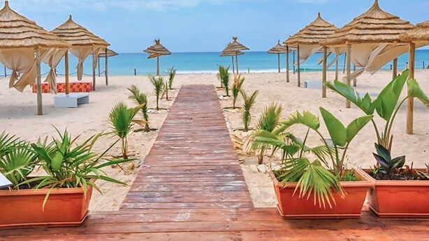 Un camino de madera que lleva a sombrillas de playa sobre una arena.
