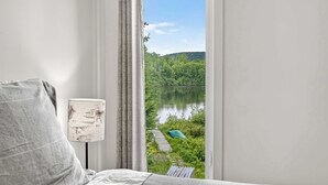 A bedroom with a view of a lake and forest, a lamp, and a bed.