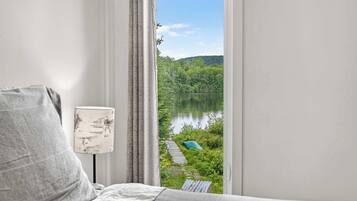 Une chambre avec vue sur un lac et une forêt, une lampe et un lit.