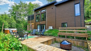 A modern two-story house with a deck, outdoor seating, and a barbecue area.