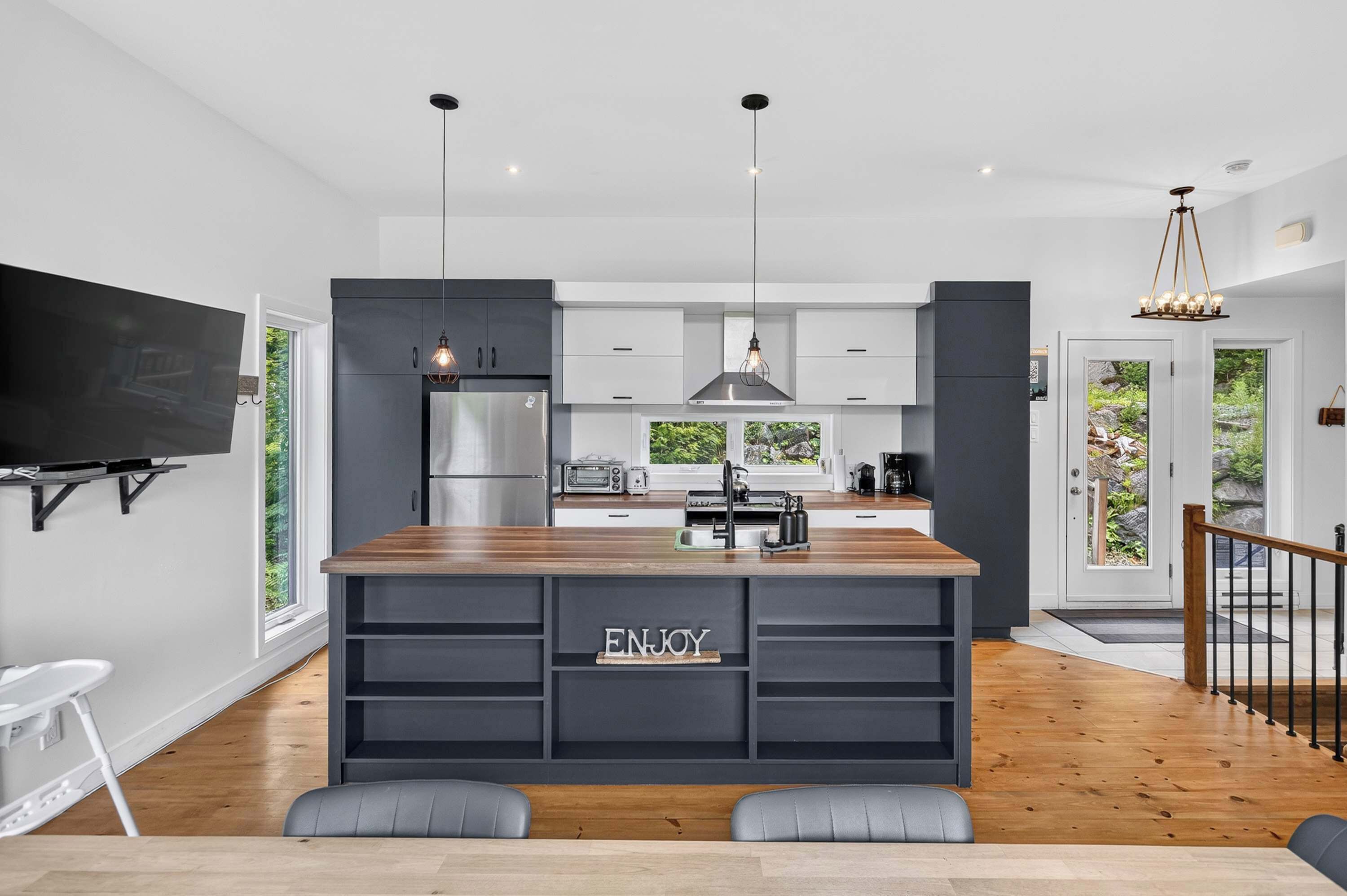 Une cuisine moderne dotée d’un îlot central, d’appareils électroménagers intégrés et d’une grande fenêtre donnant sur un espace verdoyant.