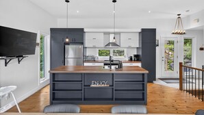 A modern kitchen with a central island, built-in appliances, and a large window overlooking greenery.