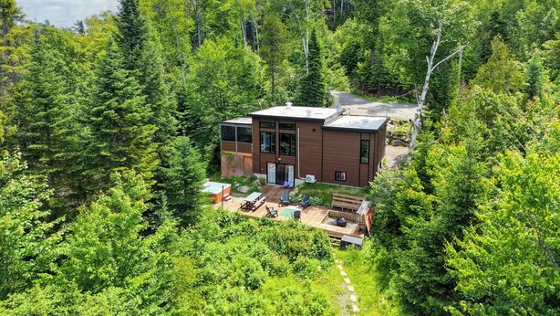 A modern cabin surrounded by dense forest, with a deck and outdoor seating area.