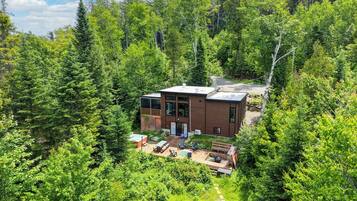 Une cabane moderne entourée d’une forêt dense, dotée d’une terrasse et d’un espace salon extérieur.