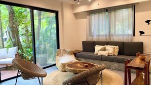 Ein modernes Wohnzimmer mit einer Couch, zwei Korbstühlen, einem runden Holztisch und einem Esstisch mit einer Schüssel.