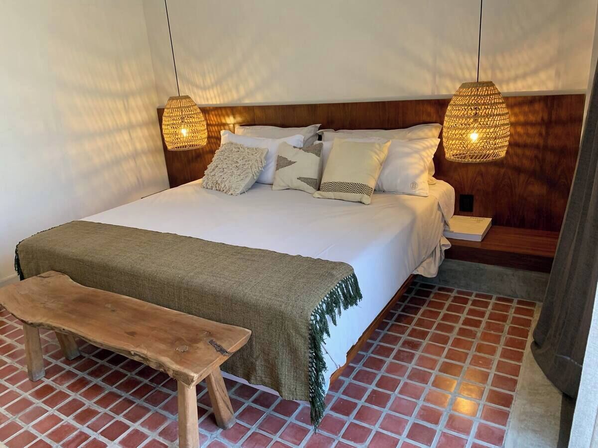 A bedroom with a wooden bed, two bedside tables, a bench, and two hanging lamps.