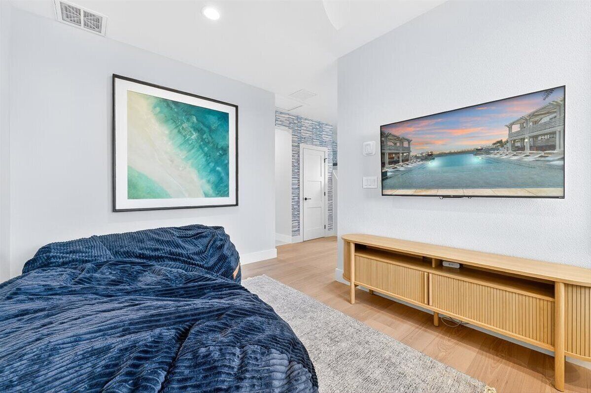 A bedroom with a bed, a TV, a painting, and a wooden console.