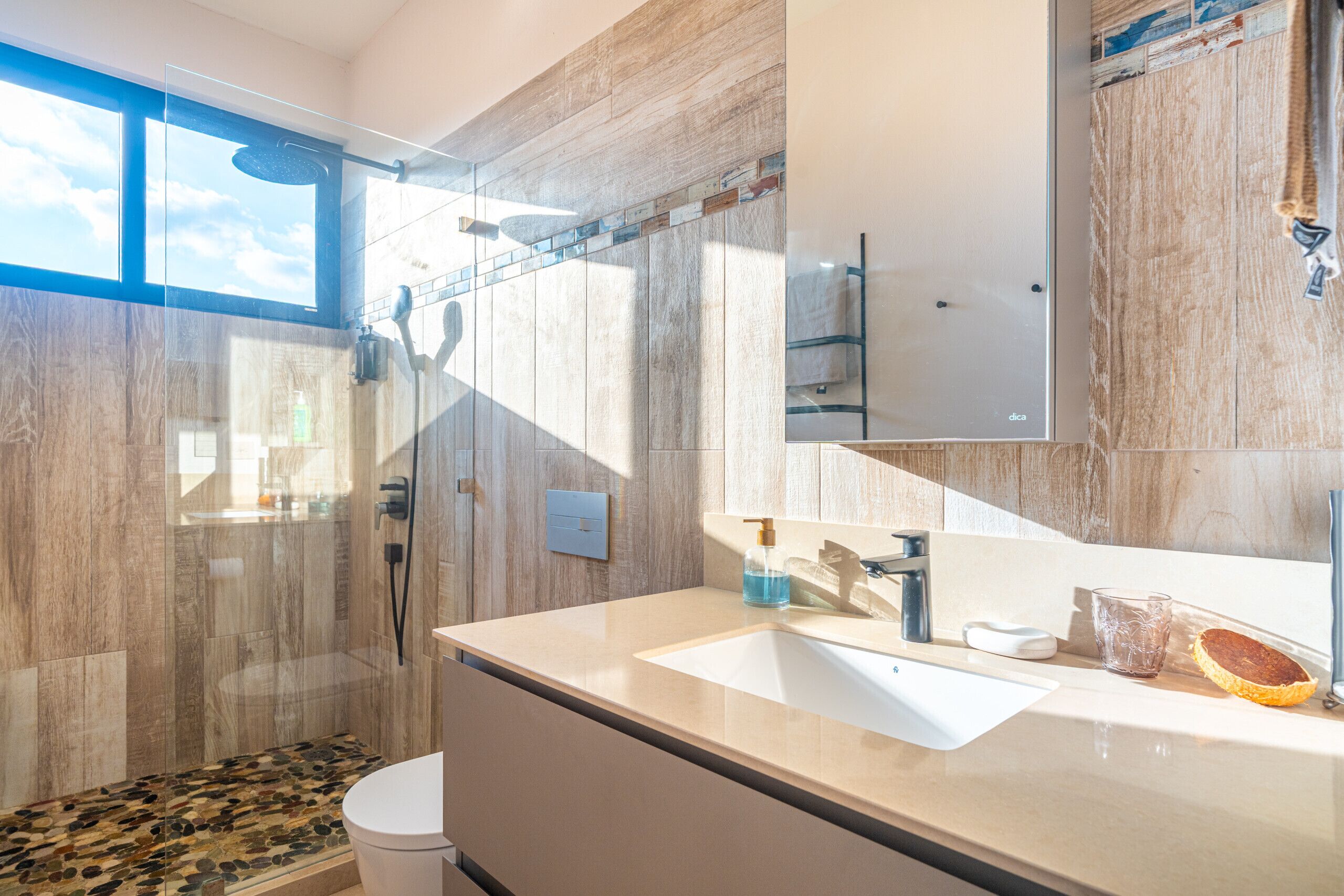 A modern bathroom with a glass-enclosed shower, a large mirror, and a beige countertop.