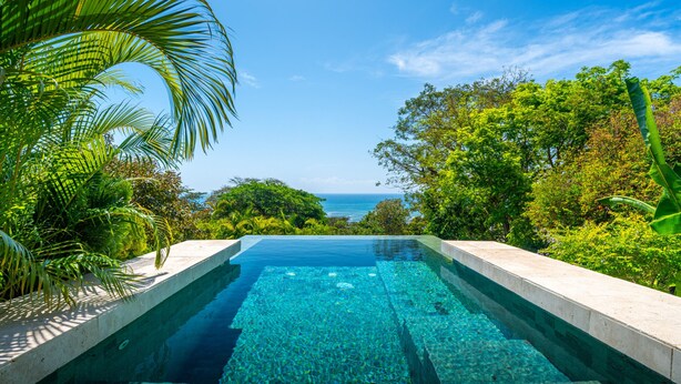 A clear swimming pool with a view of the ocean, surrounded by lush greenery. - Stealing Time Costa Rica (Parrita)
