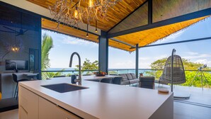A modern kitchen with a large island, a dining area with outdoor seating, and a view of the ocean. - Stealing Time Costa Rica (Parrita)
