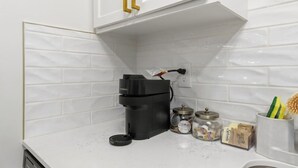 Een keuken met een witte betegelde achterwand, een koffieapparaat, potten en een kruidenrek.