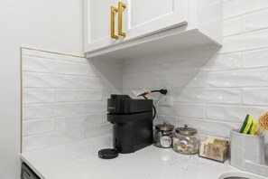Une cuisine avec un mur recouvert de carreaux blancs, une machine à café, des bocaux et un porte-épices.