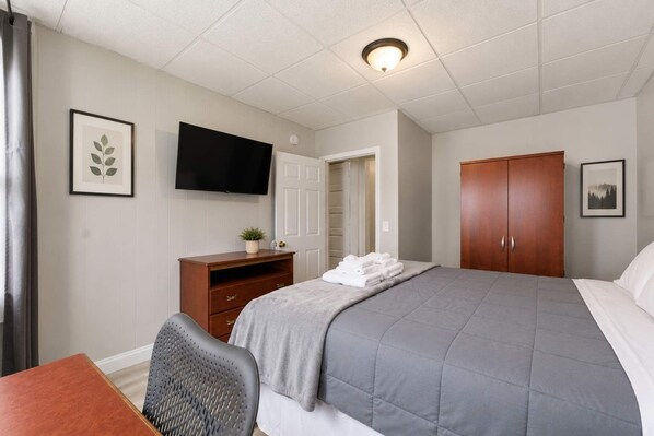 Ein Hotelzimmer mit einem Bett, einem Schreibtisch, einem Sessel, einem Fernseher, einem Kleiderschrank und einer Tür zu einem Badezimmer.