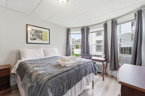 Um quarto com cama, uma cadeira, uma mesa, um radiador e uma janela com cortinas.