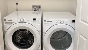 Två tvättmaskiner av märket Whirlpool, med frontmatning, står i ett tvättrum. Ovanför tvättmaskinerna finns en hylla där rengöringsmedel förvaras.