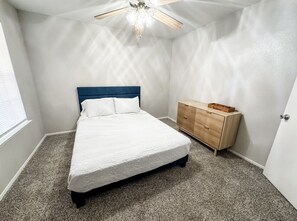 Une chambre à coucher avec un lit, une commode, un ventilateur de plafond et une fenêtre.