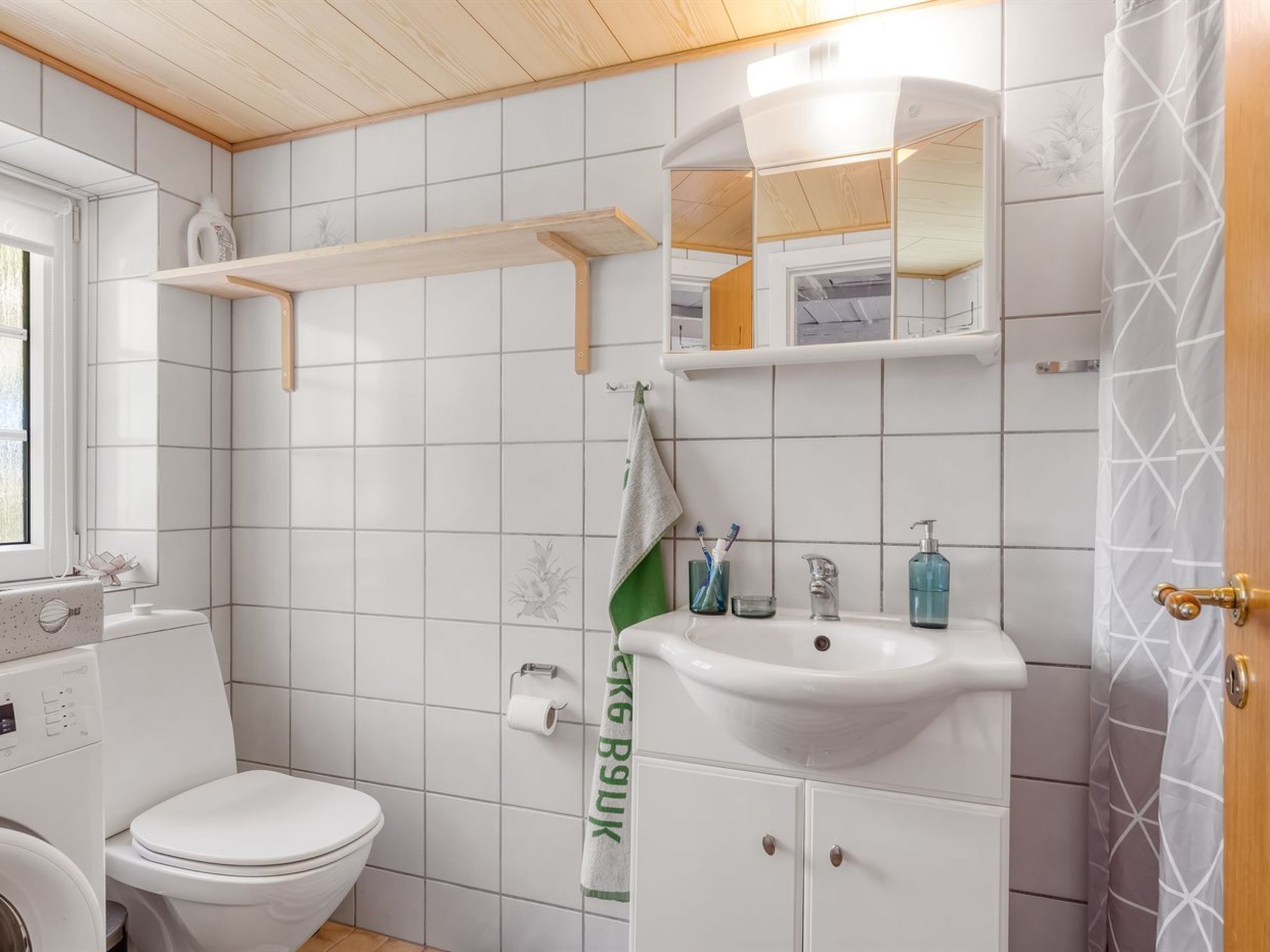 Un baño con inodoro, lavamanos, espejo y perchero para toallas.
