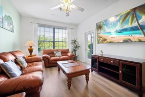 Ein Wohnzimmer mit einer Couch, einem Couchtisch, einem Fernseher und einem großen Fenster.
