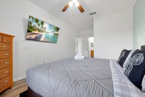 Une chambre à coucher avec un lit, une commode, un tableau et un ventilateur de plafond.