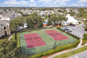 Un court de tennis entouré d’un quartier résidentiel avec des maisons et un parking.