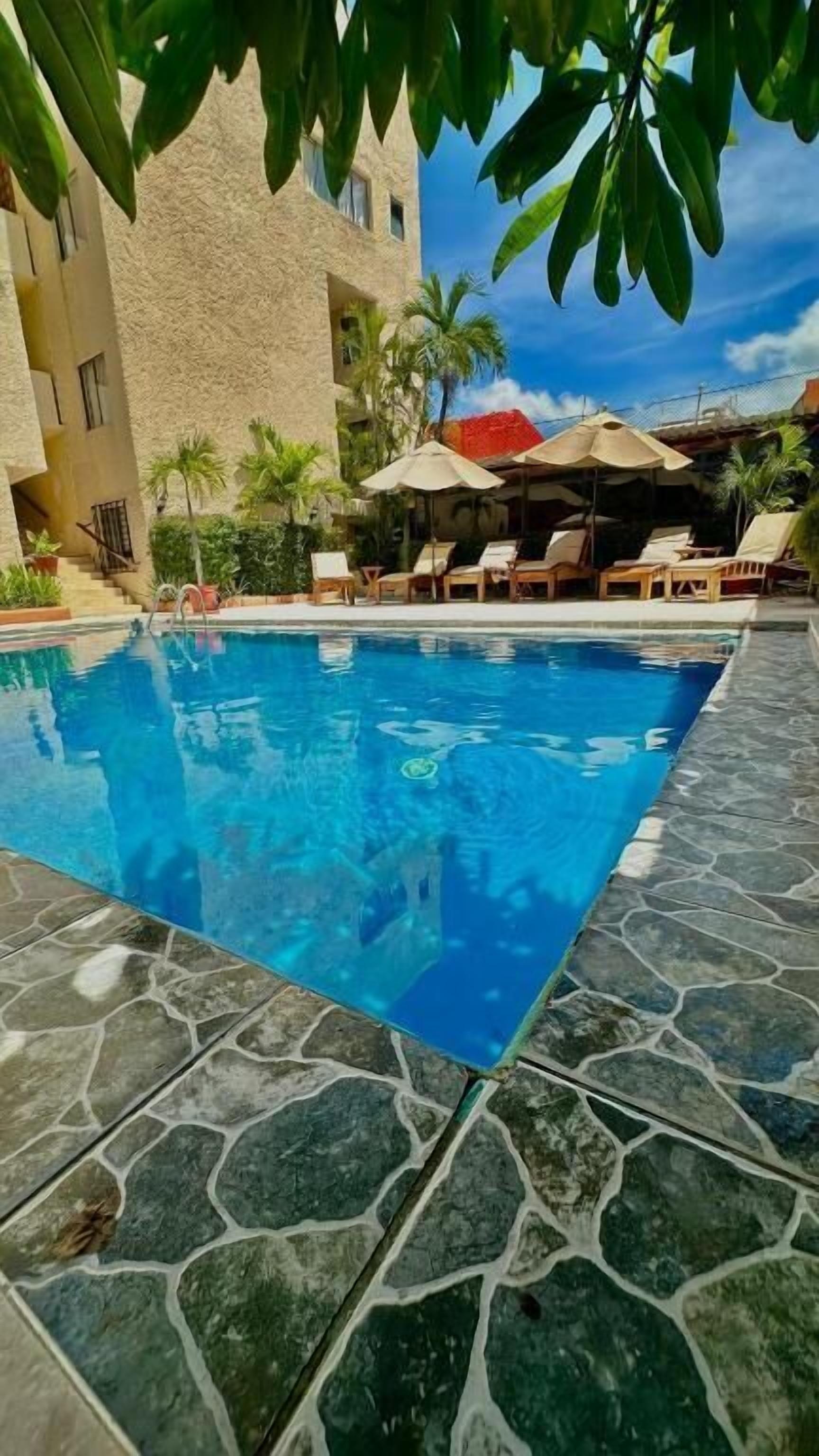 Une piscine avec des carreaux de pierre, des chaises longues et des parasols.