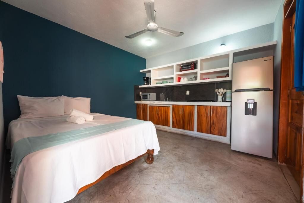Une chambre comprenant un lit, un ventilateur de plafond et une kitchenette équipée d’un réfrigérateur et d’un four à micro-ondes.