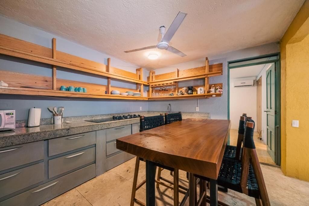A kitchen with wooden shelves, a wooden dining table, and a ceiling fan.
